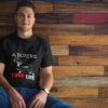 man wearing a tshirt mockup while sitting against a wooden wall a17849